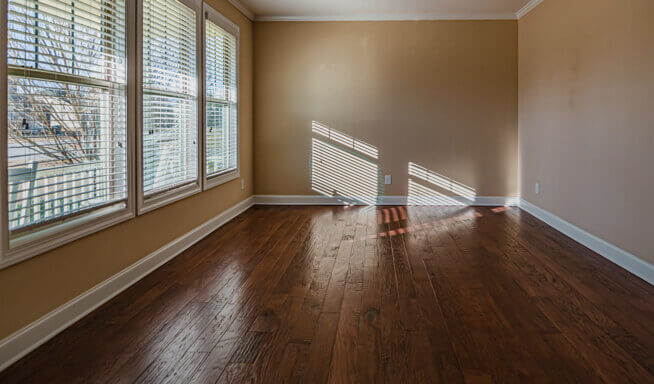 An empty bedroom inside a house, with wood floors big windows, and cream walls.